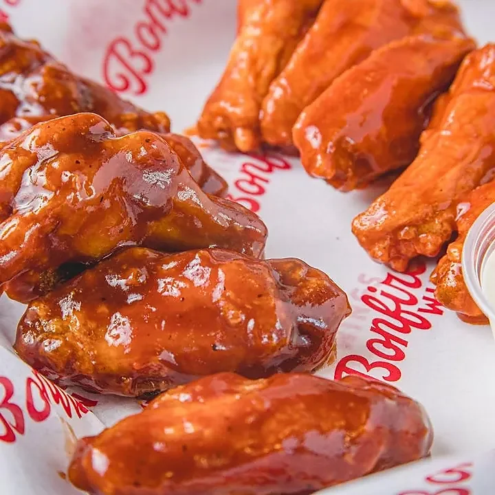 Close-up of glossy barbecue sauced chicken wings on branded paper