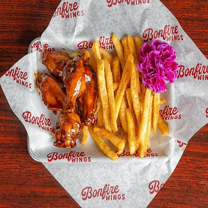 Small order of glazed wings with seasoned fries on paper