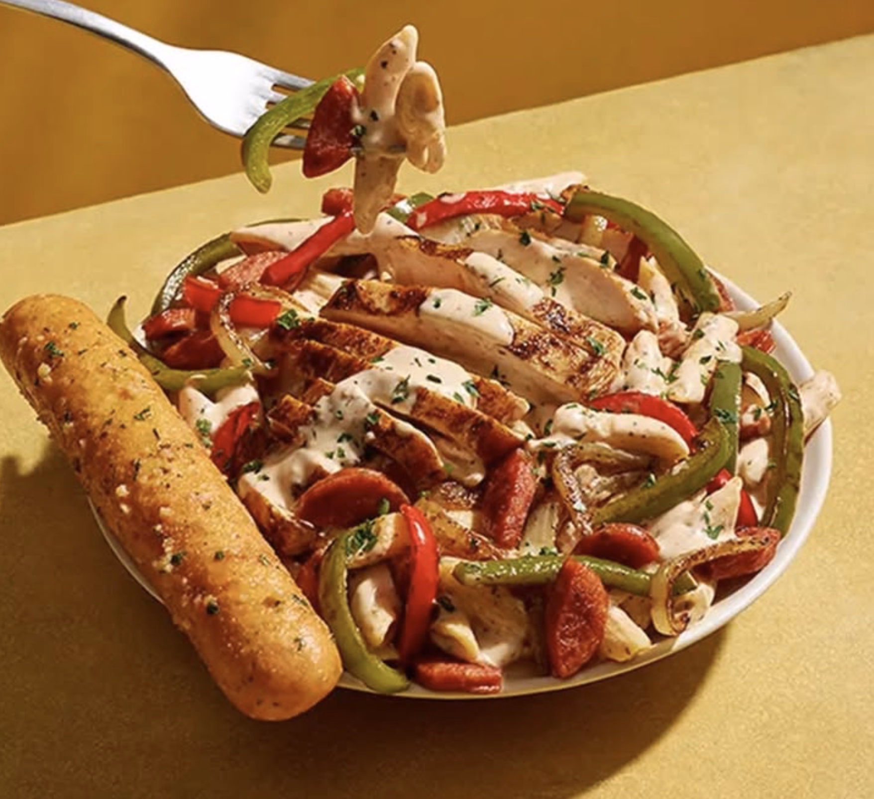 Creamy pasta with grilled chicken, bell peppers, and sausage, served with a garlic breadstick.