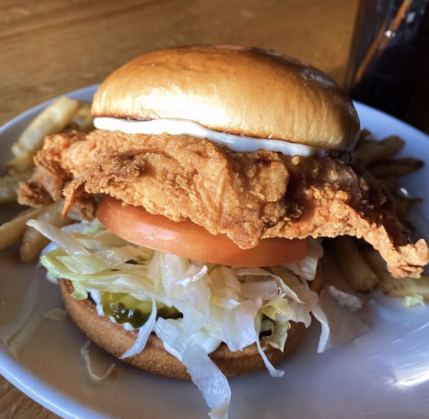 Crispy fried chicken sandwich with lettuce, tomato, pickles, and fries.