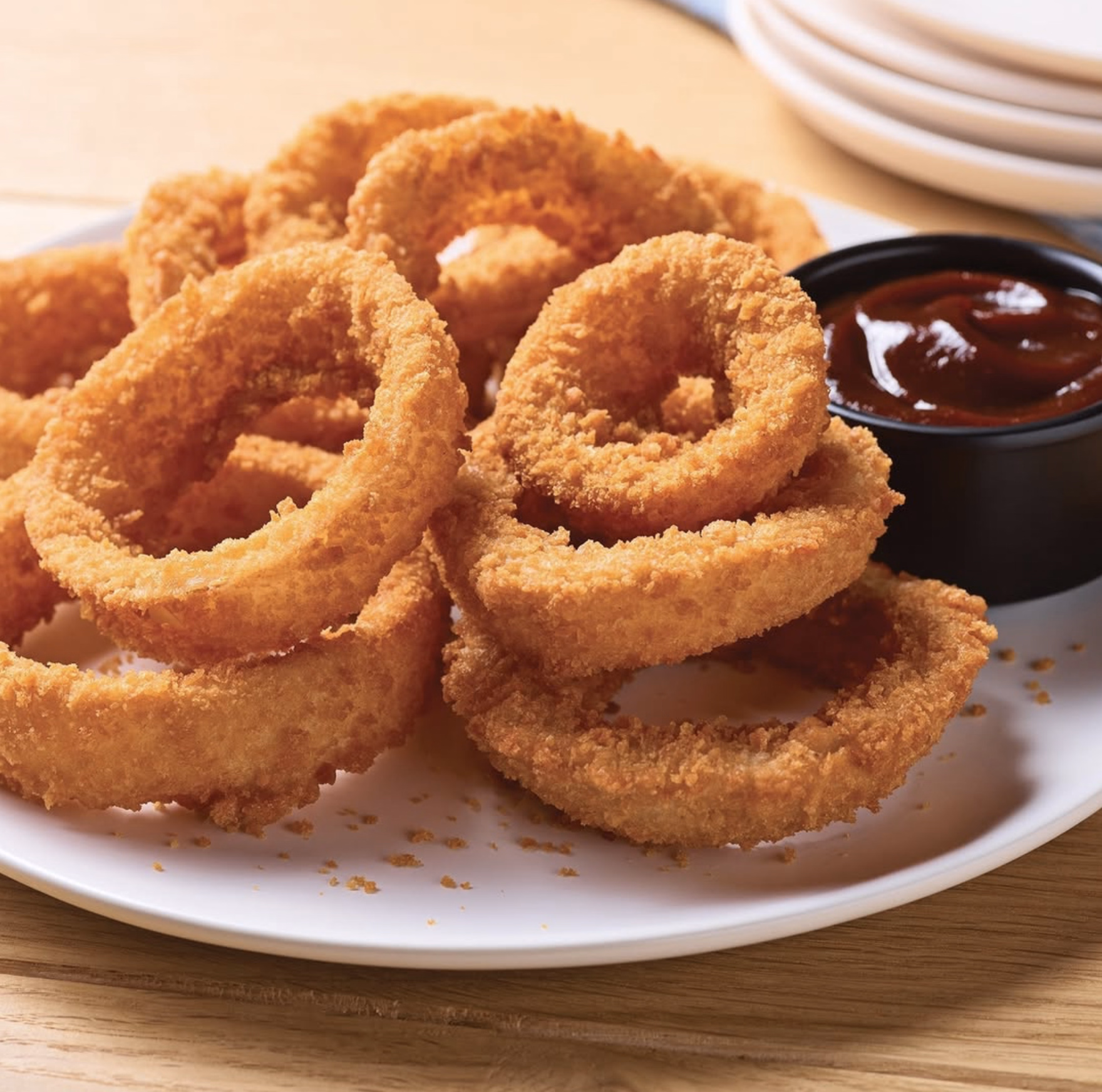 Crispy golden onion rings served on a white plate with a side of tangy dipping sauce.