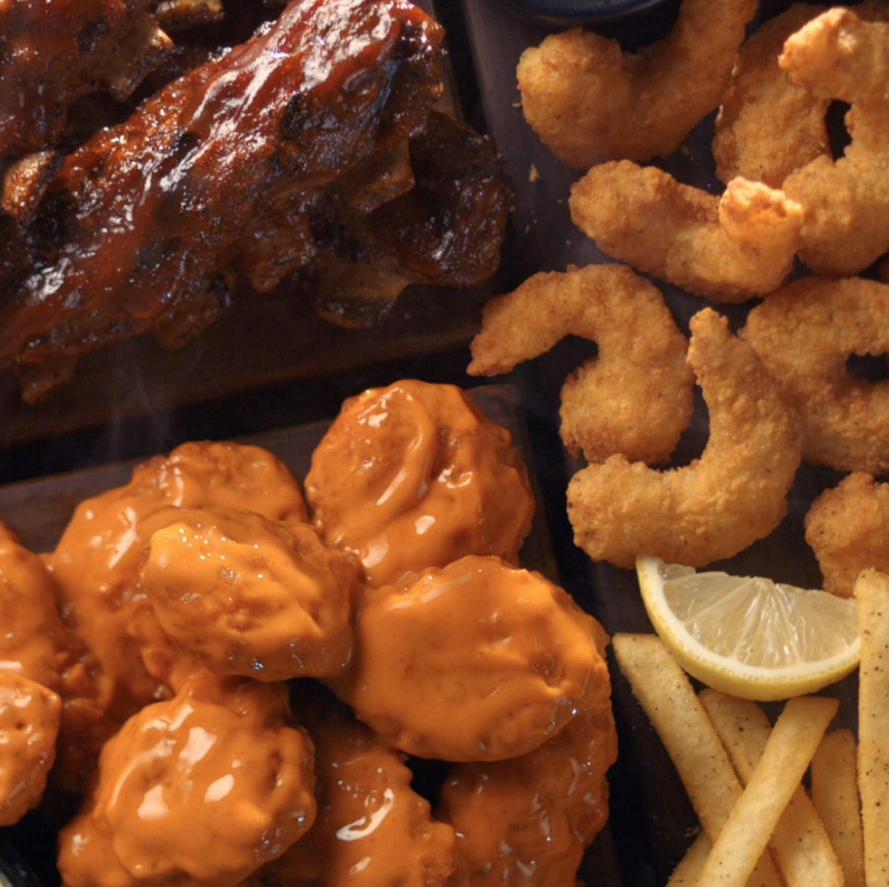 Platter of saucy wings, fried shrimp, ribs, and seasoned fries with lemon wedge.