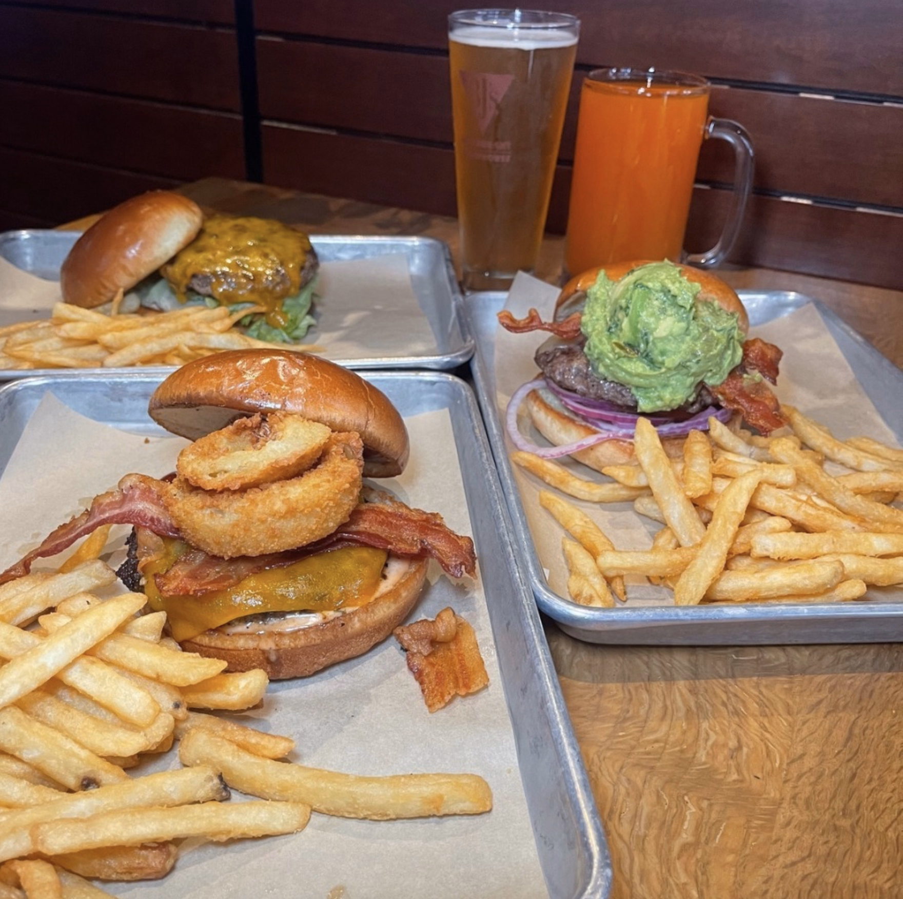 Three BJ’s gourmet burgers topped with bacon, cheese, onion rings, and guacamole, served with fries and beers.