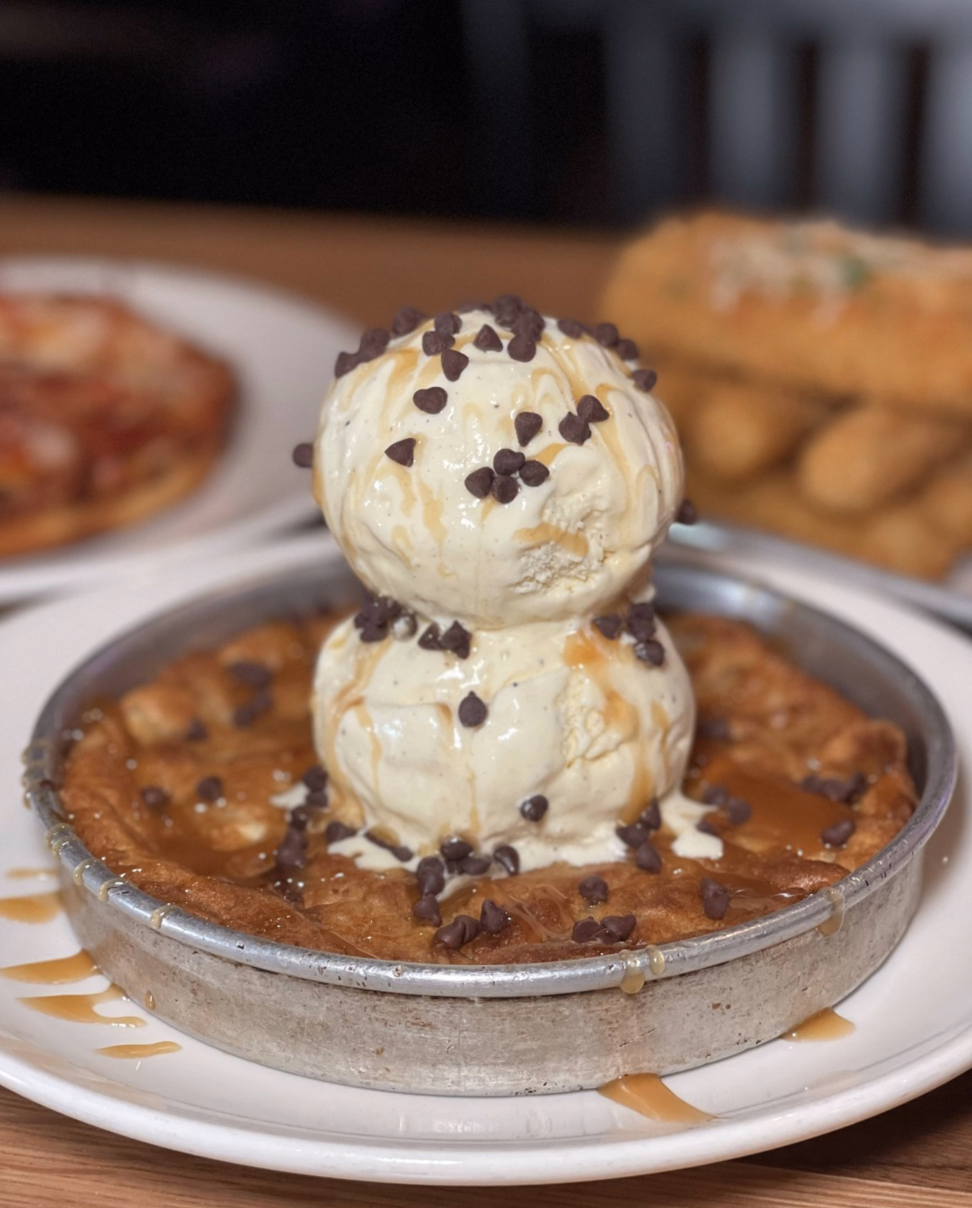 A fresh-out-of-the-oven cookie skillet dessert topped with creamy ice cream and sweet caramel sauce.