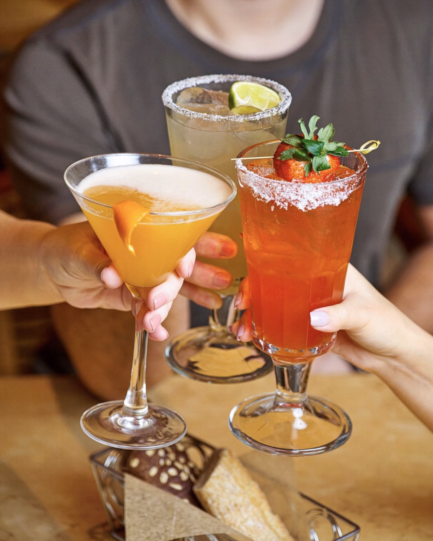 Trio of vibrant cocktails garnished with lime, strawberry, and orange peel.
