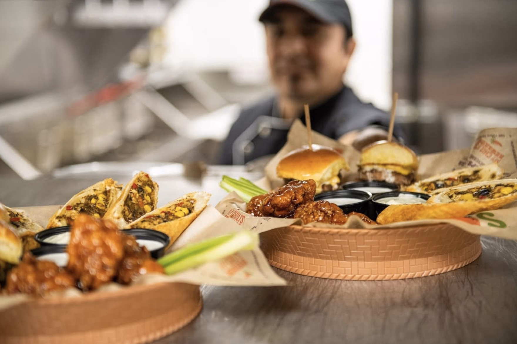 A table loaded with Chili’s shareable bites—crispy wings, mini burgers, Southwest eggrolls—served with ranch and marinara.