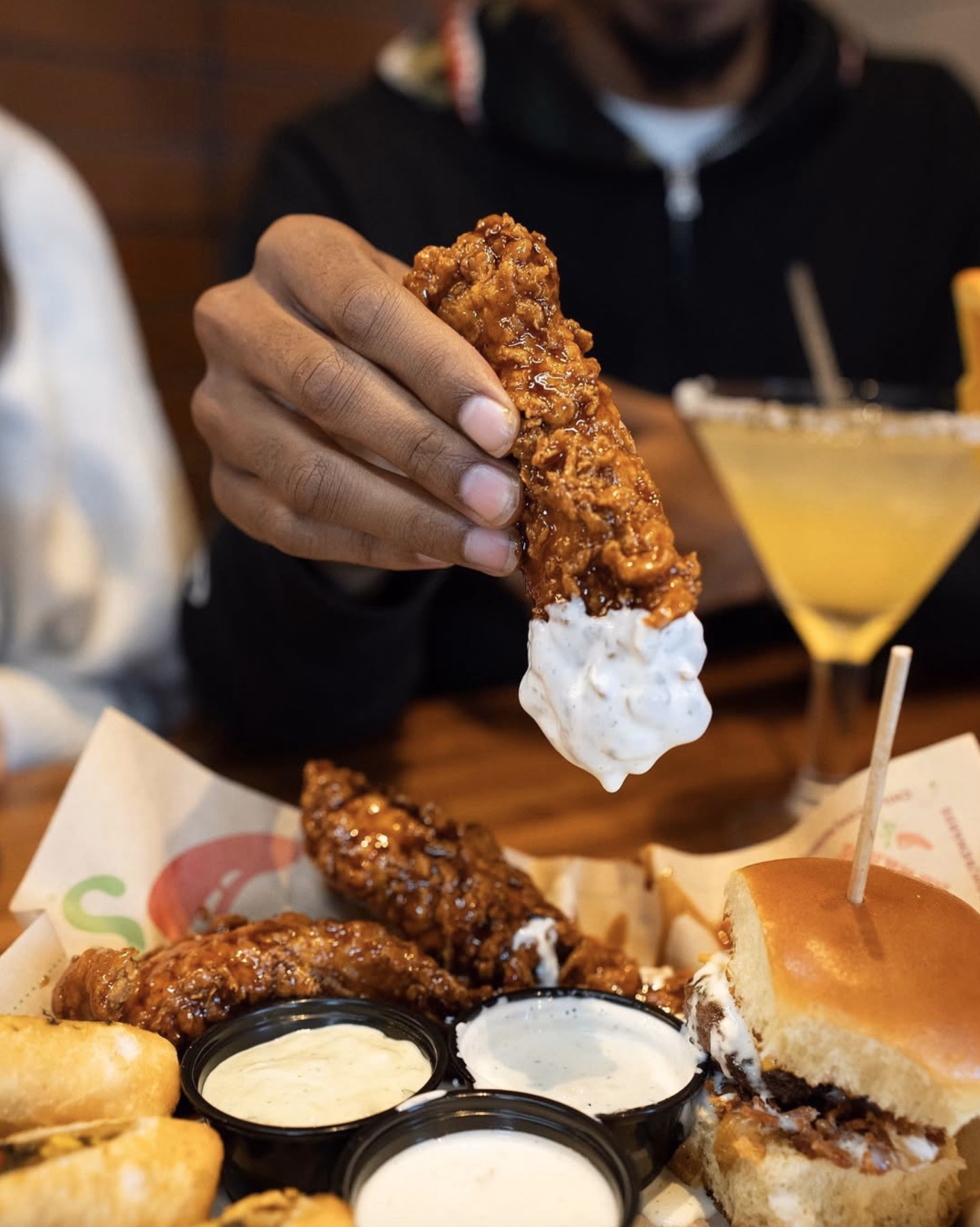 Glazed honey-chipotle chicken  at Chili’s being dipped into creamy ranch, with a slider and sauces nearby.