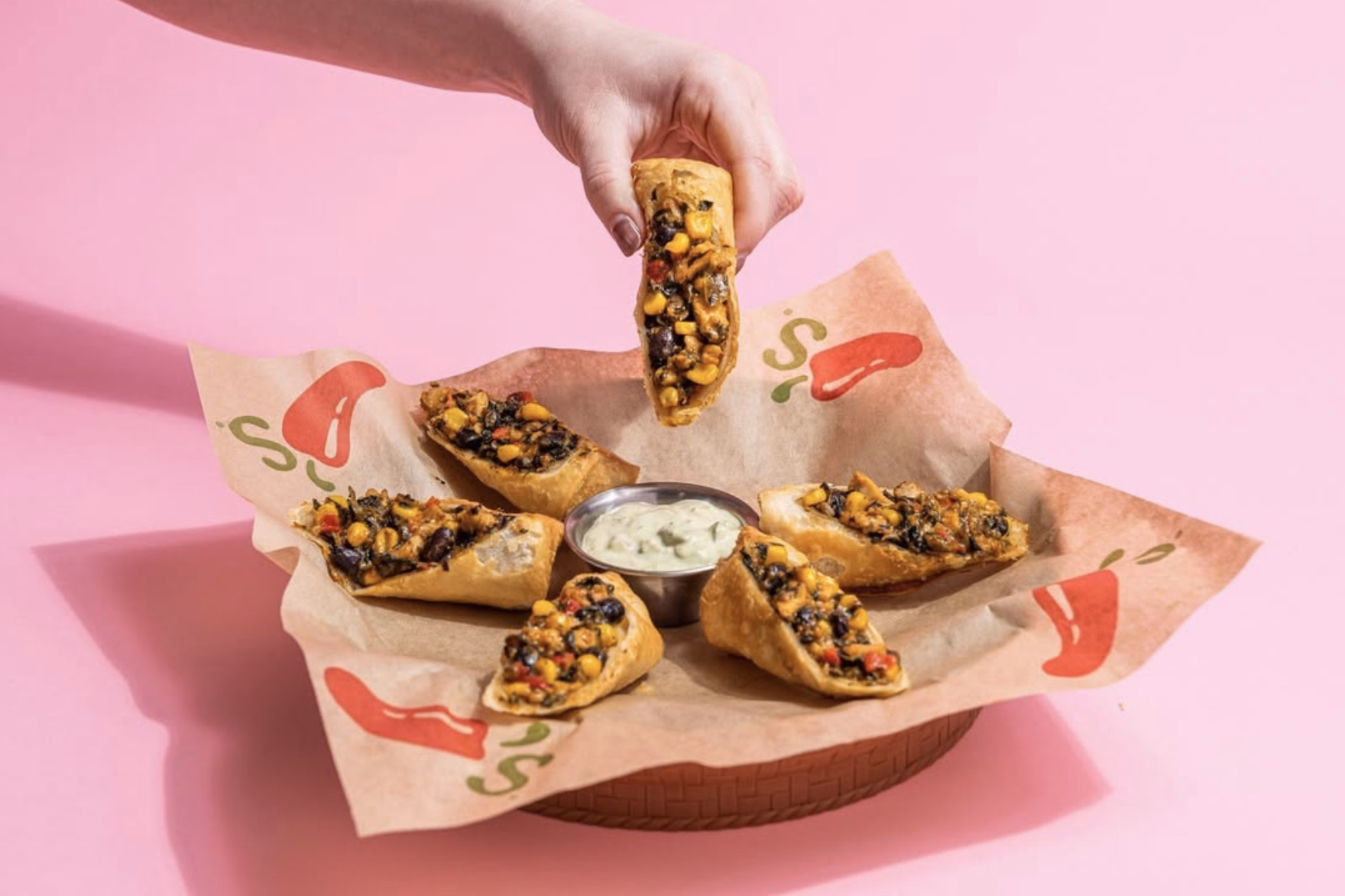 Chili’s Southwest eggrolls arranged in a circle with a creamy dipping sauce on a pink backdrop.