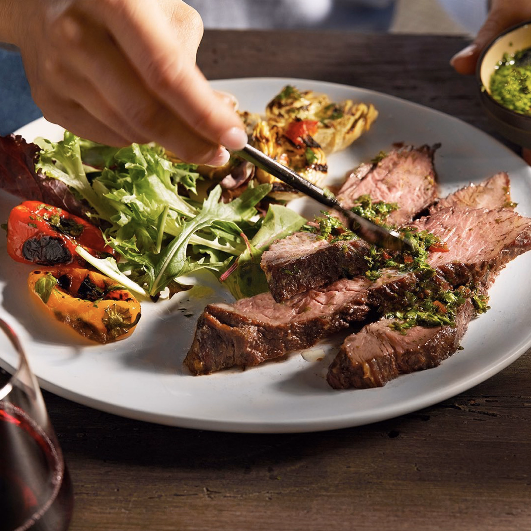 Sliced picanha steak topped with fresh chimichurri sauce, served with grilled vegetables and greens.