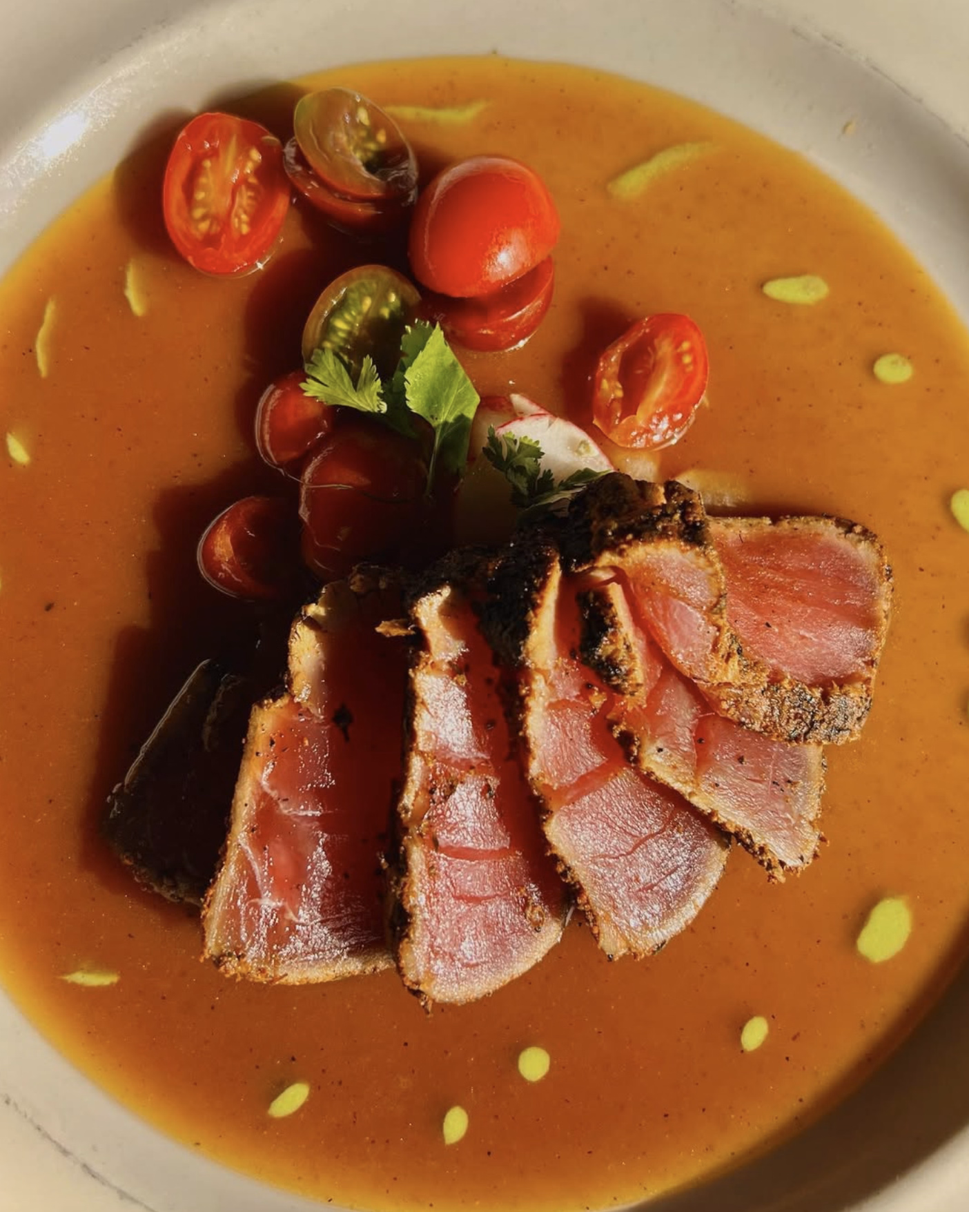 Seared ahi tuna medallions in a savory broth with cherry tomatoes and cilantro.