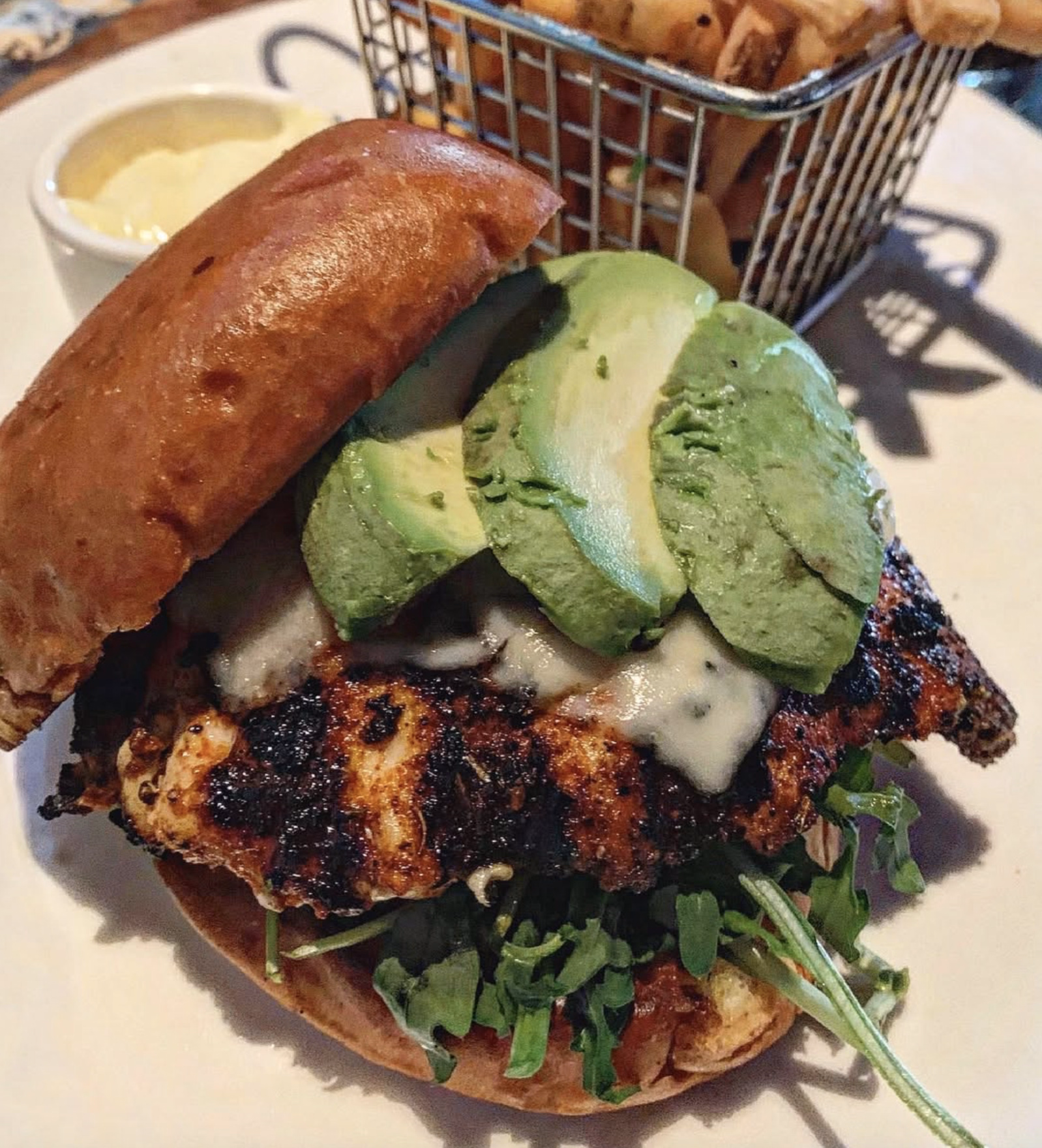 A toasted brioche sandwich with grilled chicken, avocado, and cheese, paired with crispy fries.