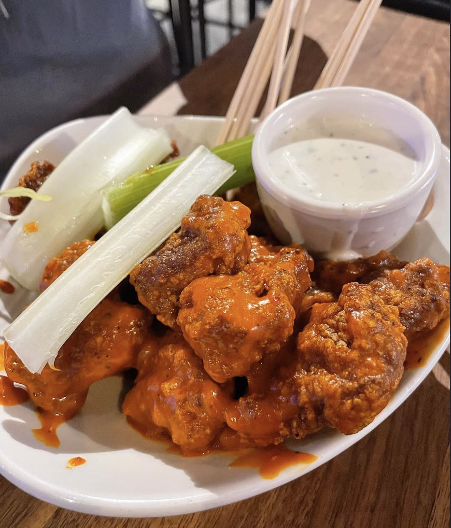 A plate of spicy buffalo boneless wings with crunchy celery and a cup of ranch dip.