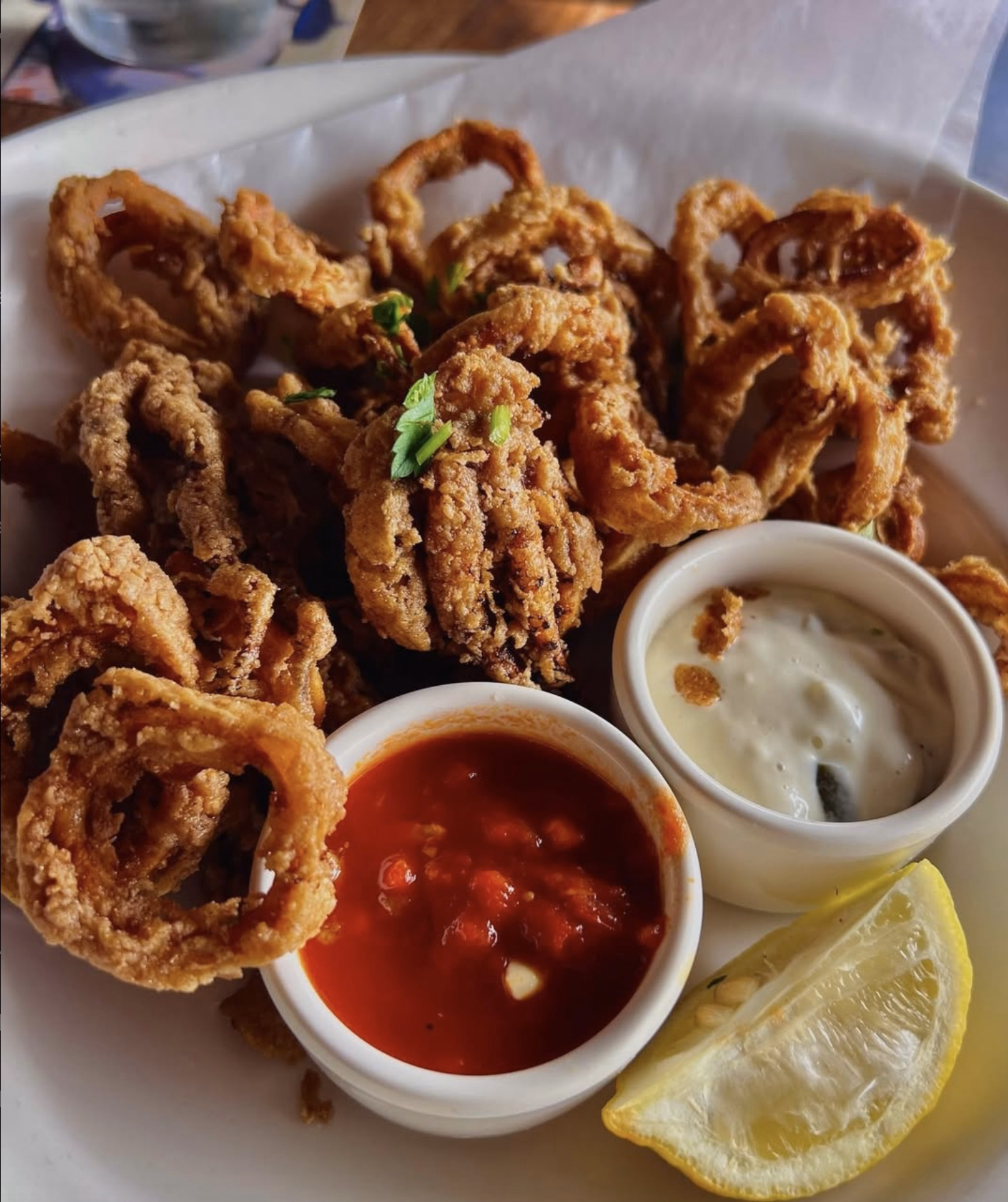 Golden fried calamari with two dipping sauces and a lemon wedge.