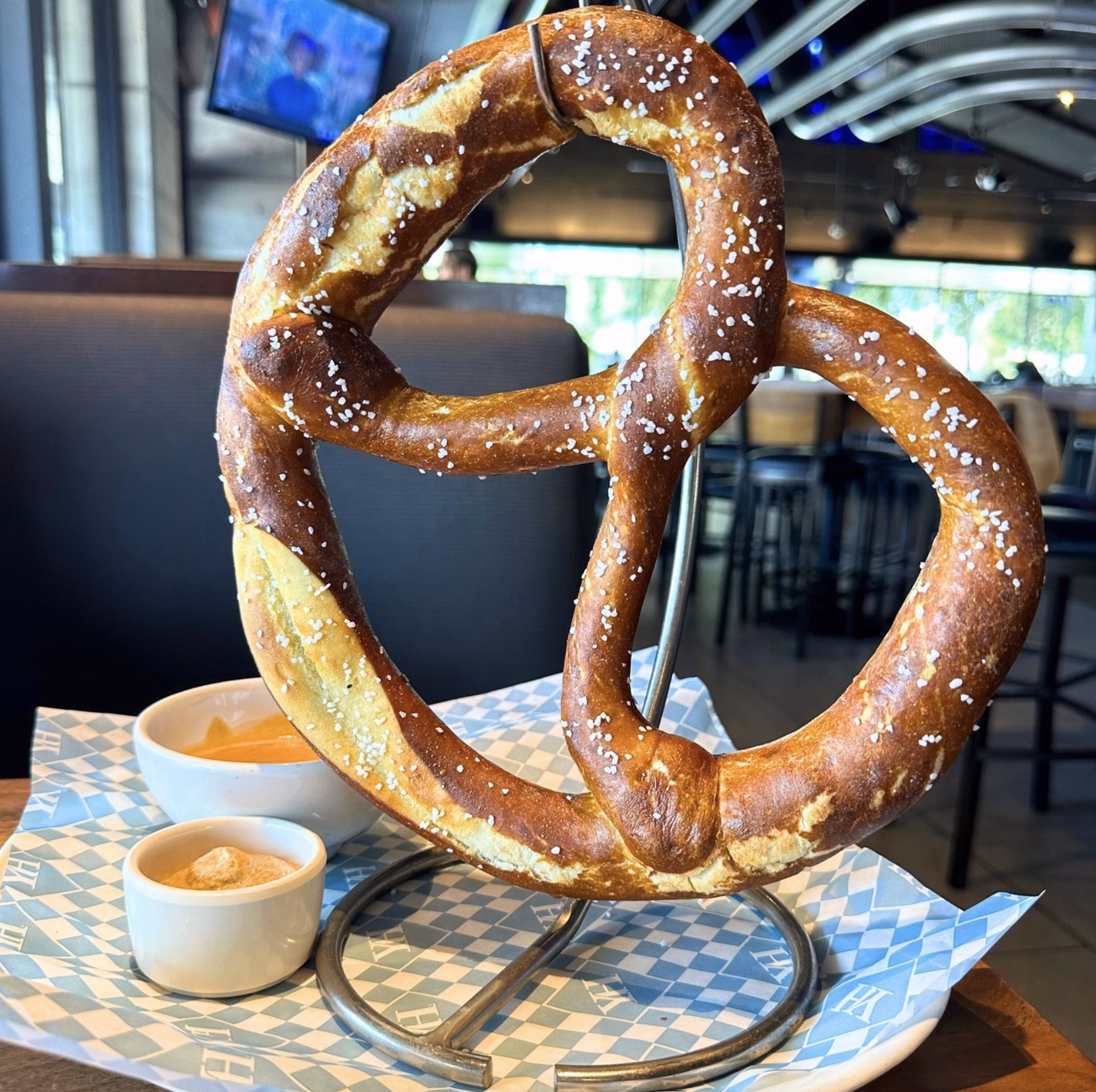 A warm pretzel on a metal stand accompanied by beer cheese and mustard dip.