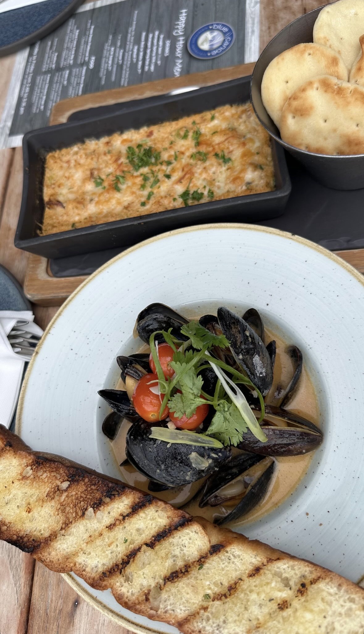 Mussels in broth, cheesy dip, and crackers on a wooden table.