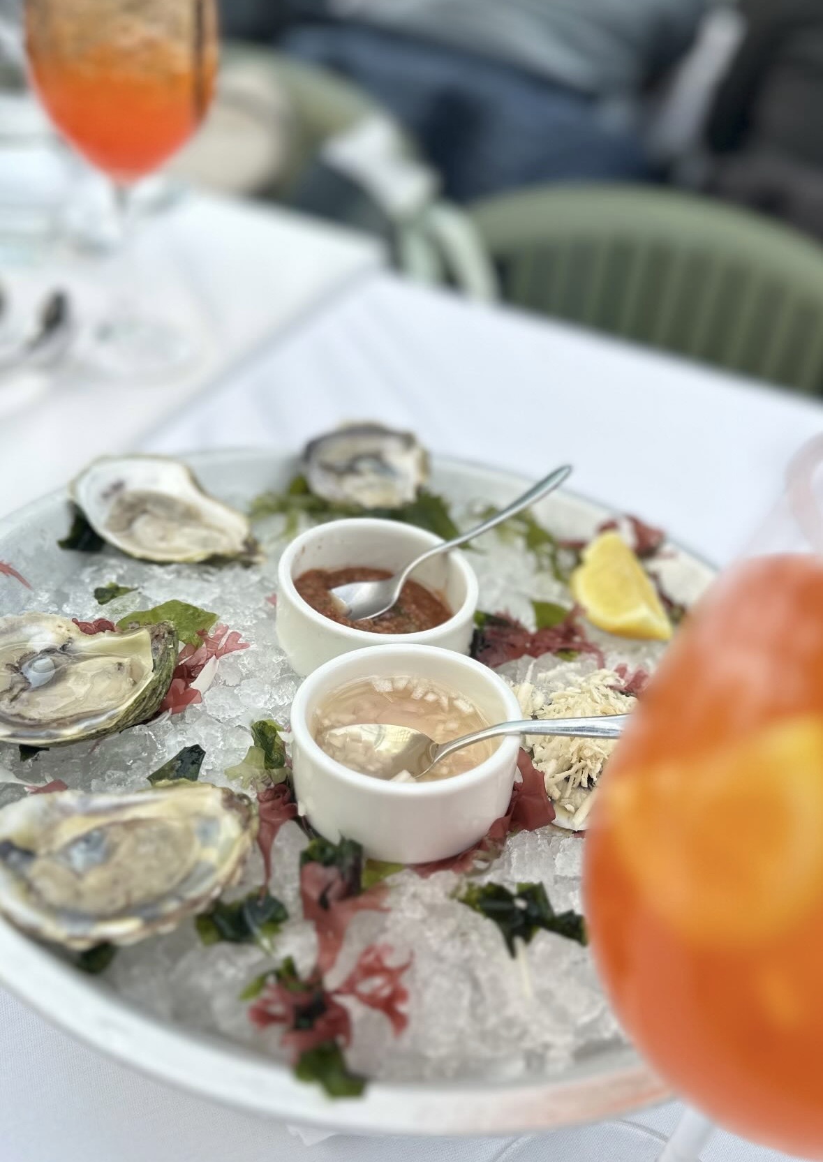 Oysters on ice with sauces, seaweed, lemon, and a drink.